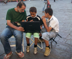 Hombre en una plaza conultando un portátil con dos niños.